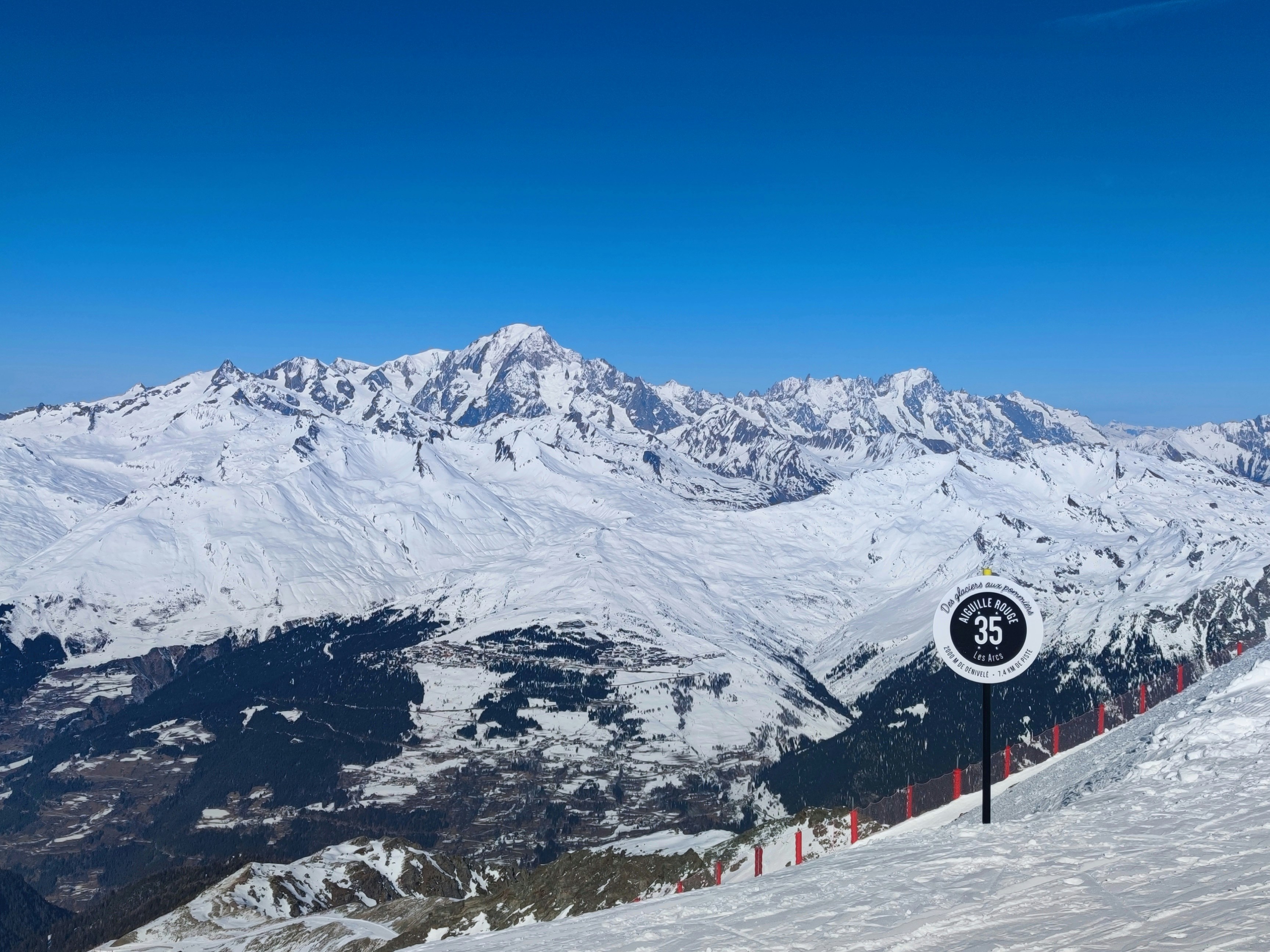 Snowy mountain panorama from Aiguille Rouge in Les Arcs with a piste marker in the foreground